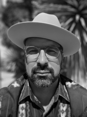 Black and White headshot photo of Marvin González De León wearing glasses and a brimmed hat