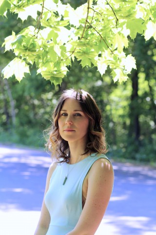 Headshot photo of Sofya Levitsky-Weitz in a blue dress standing under a branch full of bright green leaves