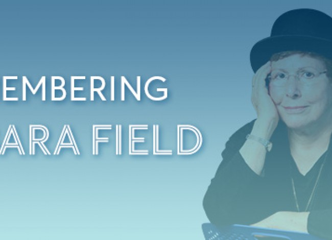A light blue box with the words REMEMBERING BARBARA FIELD on it. An image of Barbara is to the left of the text. She is sitting in a chair, wearing a black shirt and hat. Her right hand rests on her face. Her left hand rests on the chair.